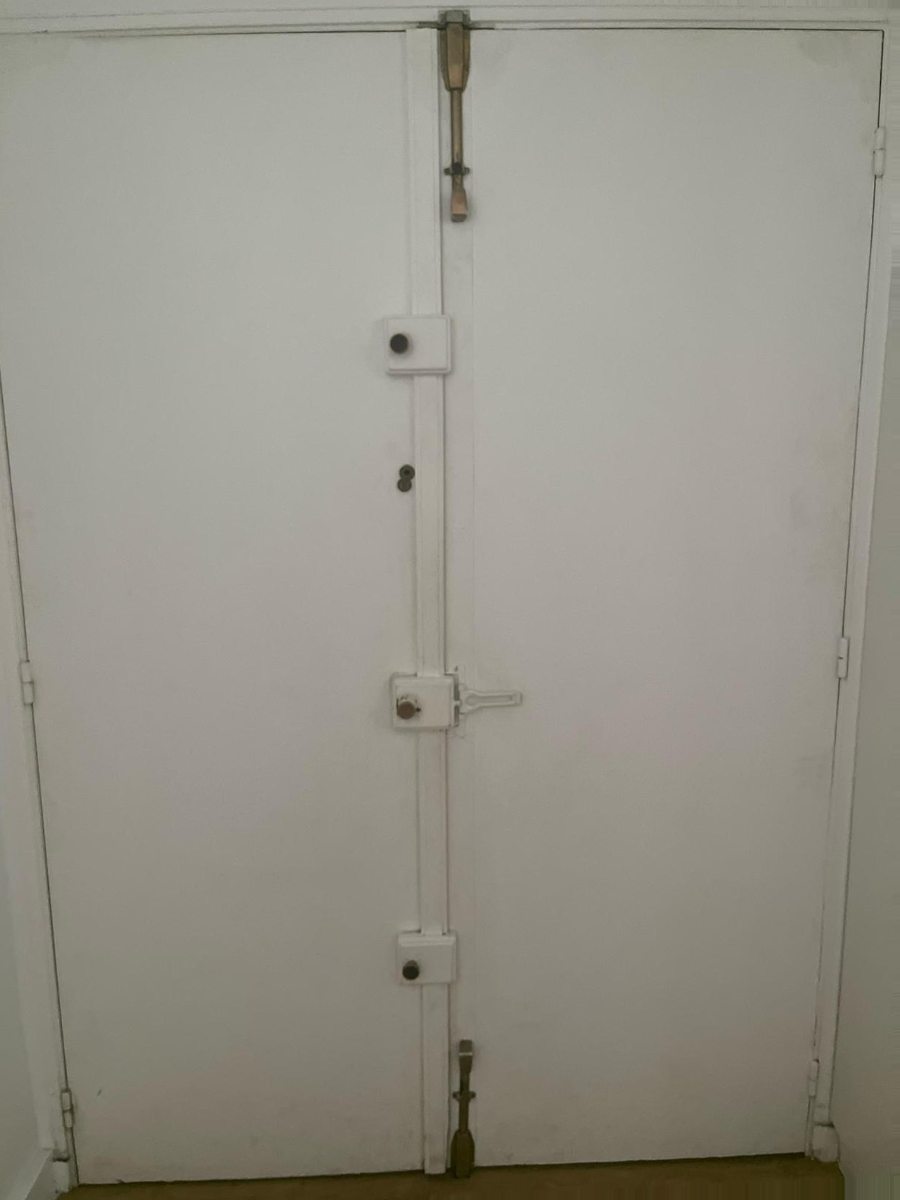 Porte double avant l'intervention : serrure en applique et barres verticales